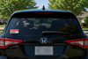 Rear view of a black Honda minivan with a red and white 'DOGS' warning sticker on the left side of the back window, parked outdoors with trees and a house in the background.