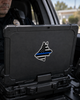 A black hard case with a Thin Blue Line dog silhouette sticker on the lid, shown inside a vehicle with a police officer partially visible in the background.